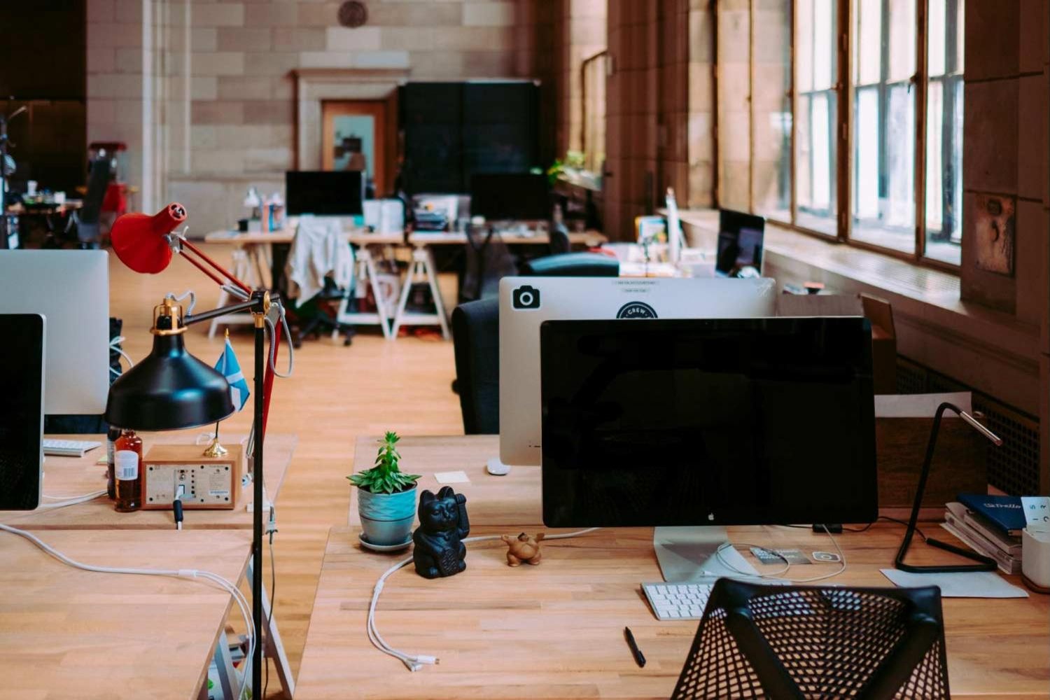 An open-plan office with desks and monitors beside tall windows